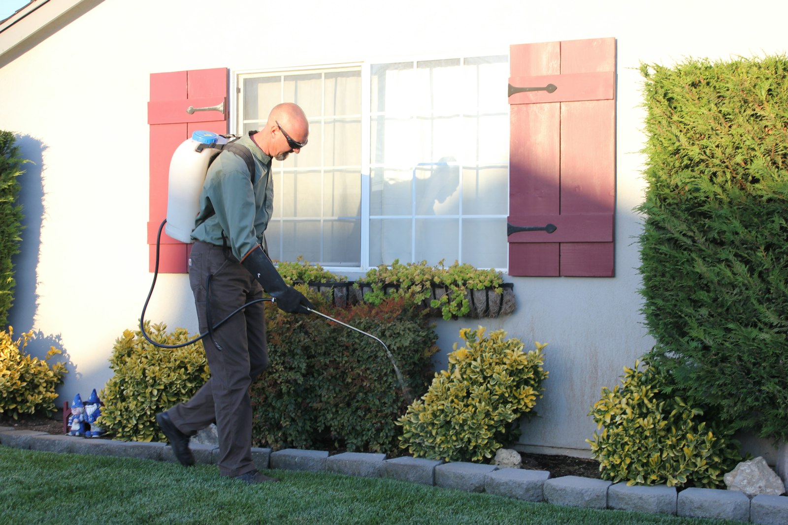 A pest control technician with equipment in front of a house